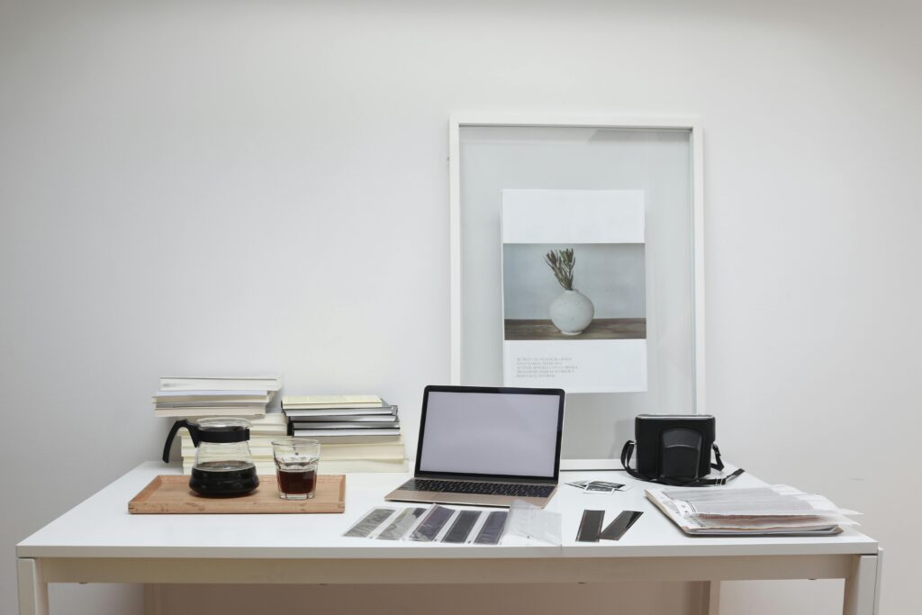 Modern laptop with blank screen arranged with retro filmstrips photo camera and framed picture placed on table near coffee and stack of books